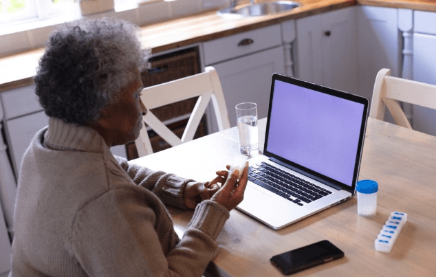 senior woman sitting at a table with laptop and prescriptions