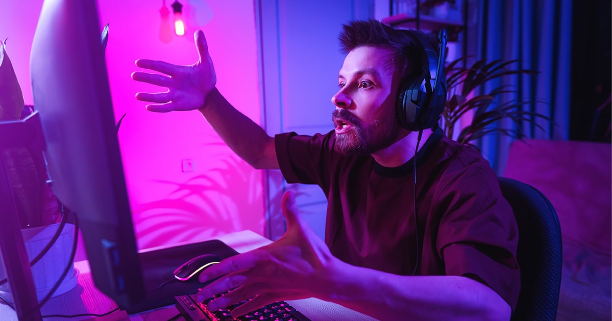 Young white man, online gamer in pink light frustrated at the computer