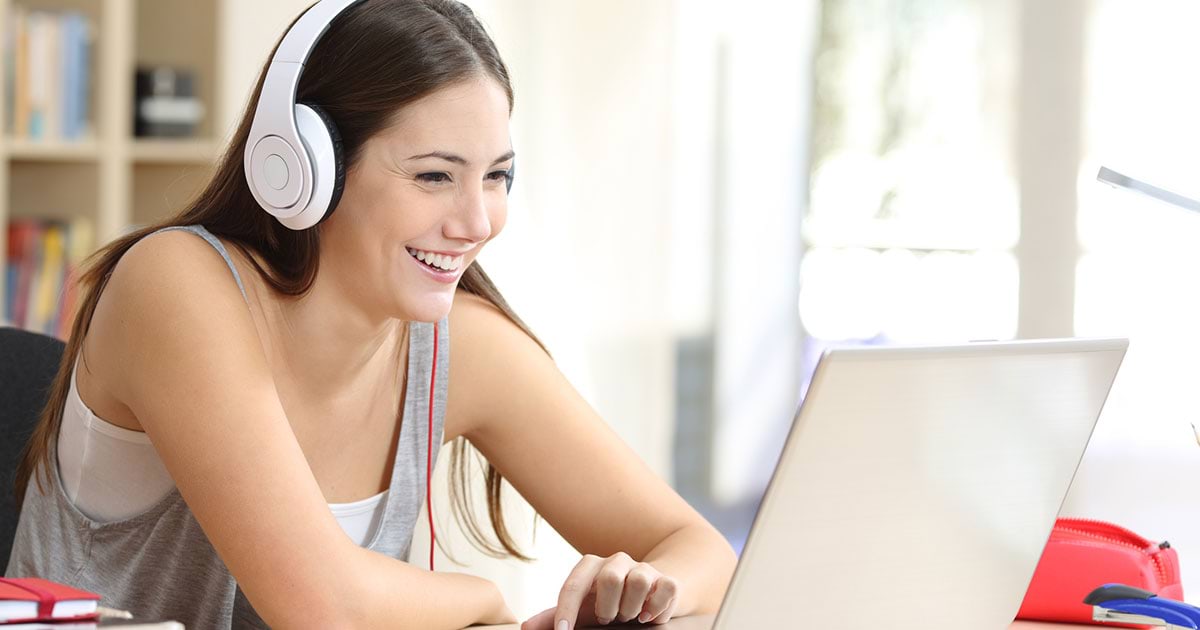 A student with headphones laughs while using laptop