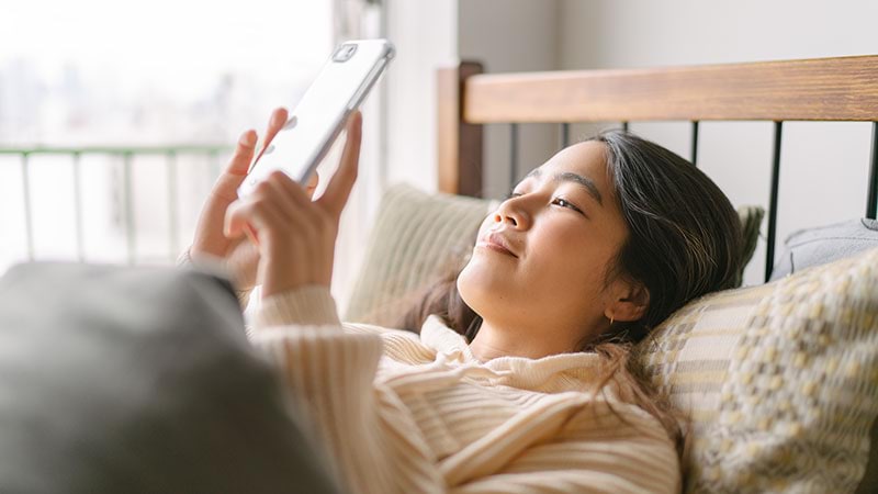 A woman looks at her smartphone in bed