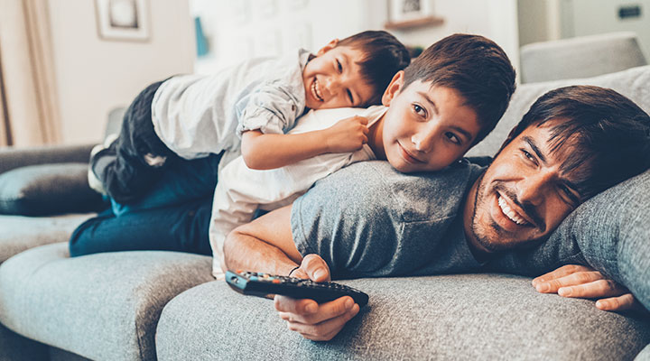 A man watches TV on the couch with his two kids