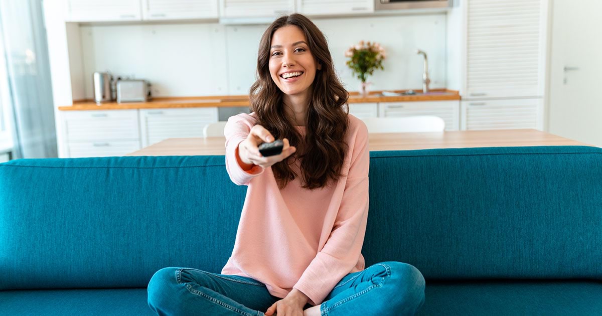 A smiling woman points her remote control at the TV